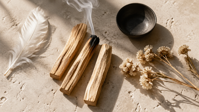 Bâtons de Palo Santo posés sur surface en pierre claire avec fumée blanche et fleurs séchées