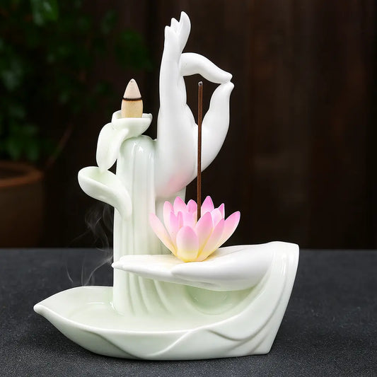 Brûleur d’encens en céramique blanche en forme de main tenant un lotus rose, compatible cônes et bâtons, sur fond ardoise et décor végétal.