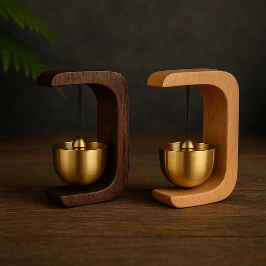 Deux cloches zen en laiton suspendues dans des supports en bois clair et foncé, posées sur une table en bois sombre avec fond ardoise