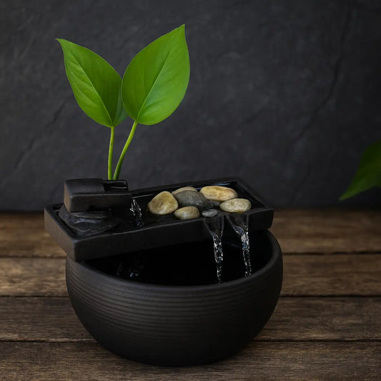 Fontaine de table zen en céramique noire avec cascade d’eau, galets décoratifs et plante verte sur fond bois et ardoise