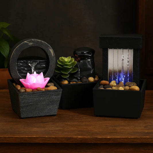 Trois fontaines décoratives de table avec lotus lumineux, cascade rocheuse et chute rectangulaire LED bleue, éclairées avec une luminosité équilibrée sur table bois.